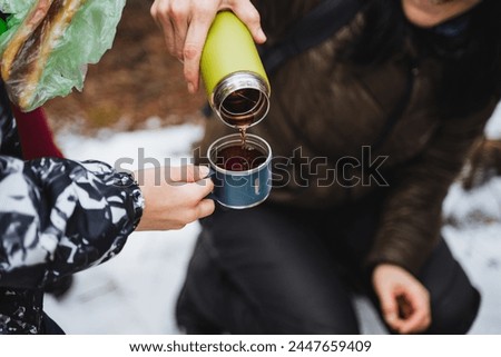 Pouring tea from a thermos into a mug in nature, hiking in the forest, hot drink pouring into a glass, tourist utensils, friendship, joint action. High quality photo