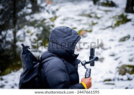 Profile photo of unrecognizable young man in black coat and hood filming snowy forest scene. Royalty-Free Stock Photo #2447661595