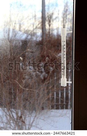 A plastic retro thermometer outside the window of a village house on a frosty day. View from the window into the courtyard, vertical photo