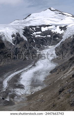 A photo with a view of a part of the Grossglockner mountain covered with snow and a glacier against a stormy sky in the Hohe Tauern National Park, Tyrol, Austria