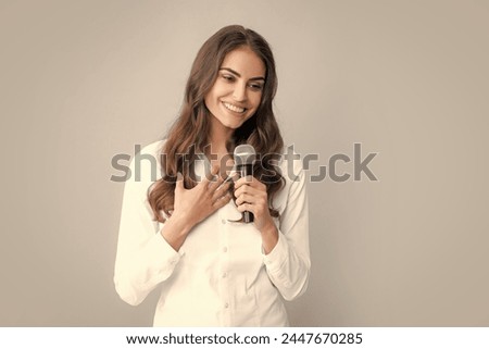 Stylish girl singing songs with microphone, holding mic at karaoke, posing against gray background.