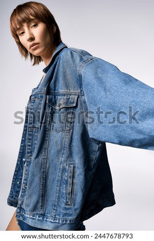 A young woman with short hair is confidently posing for a picture in a studio, wearing a trendy jean jacket.