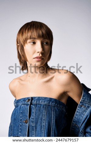 A young woman with short hair strikes a pose in a denim shirt for a portrait in a studio setting.