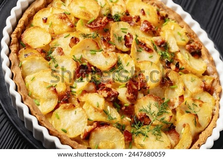 Irish potato pie of crispy crust layered with potatoes, bacon, dill and onion in baking dish on black wooden table, dutch angle view, close-up Royalty-Free Stock Photo #2447680059