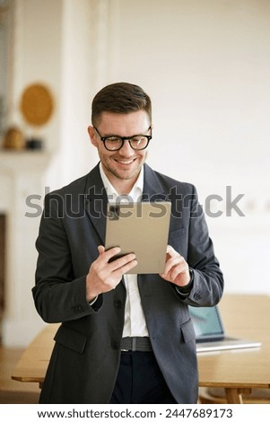 A debonair businessman engages with his tablet, his stylish eyewear and suit indicating a blend of classic fashion and cutting-edge technology in his professional life.

 Royalty-Free Stock Photo #2447689173