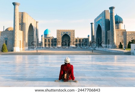 tourist woman with hat and dress red sitting on Registan, an old public square in the heart of the ancient city of Samarkand, Uzbekistan. Royalty-Free Stock Photo #2447706843