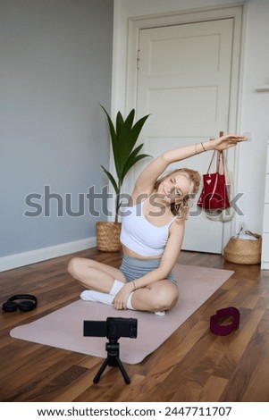 Portrait of young blogger, yoga content creator, showing exercises, recording video of herself working out at home on rubber mat. Royalty-Free Stock Photo #2447711707