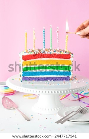 A hand lighting a candle on top of a decorated rainbow birthday cake. 
