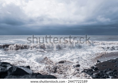 Stormy ocean waves crashing on a rocky beach with dark clouds. Rough, choppy waves meet moss-covered rocks in this dramatic scene. Suitable for websites, blogs, social media.