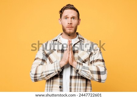 Young Caucasian man he wearing brown shirt casual clothes holding hands folded in prayer gesture, begging about something isolated on plain yellow orange background studio portrait. Lifestyle concept Royalty-Free Stock Photo #2447722601