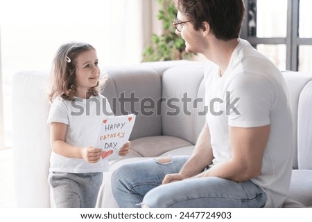 Smiling loving caring little kid daughter giving her young father greeting card, gift, present for celebrating father`s day. Family time, I love you dad! Parenthood and fatherhood concept