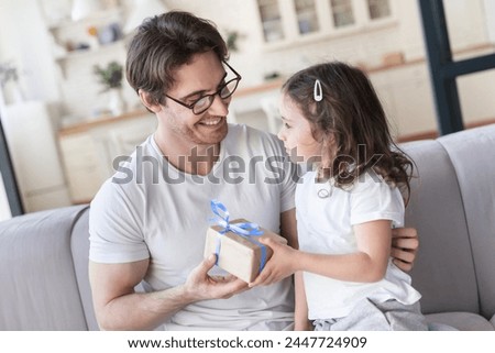 Close up image of a caring cute little kid small daughter giving her daddy a present to congratulate with father`s day, birthday. I love you, dad! Family holiday, parenthood, fatherhood