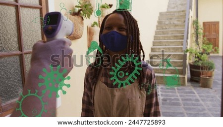 Image of virus icons over african american woman with face mask taking temperature. hobby during covid 19 pandemic concept digitally generated image.