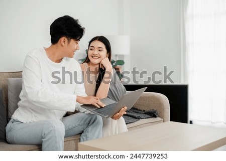 Young couple enjoys a personal moment while working on a laptop in a clean, minimalist living room with natural light.