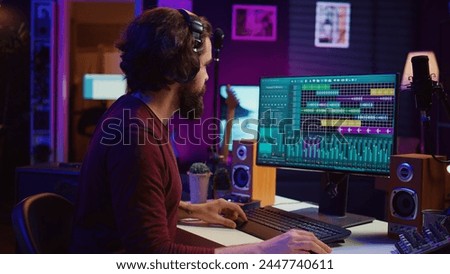 Music composer producing soundtracks using stereo panel controls and soundboard, twisting pre amp knobs for mixing and mastering tunes. Sound engineer adjusting volume in home studio. Camera B. Royalty-Free Stock Photo #2447740611