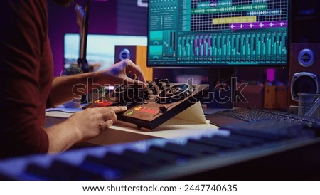 Artist editing sounds on mixing console in home studio, operating professional audio equipment to adjust volume levels on track recordings. Musician works with daw software an pre amp knobs, Camera B.