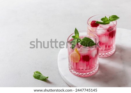 Raspberry cocktail with ice in a glass on a marble and a light background. A refreshing berry drink with mint and lemon.