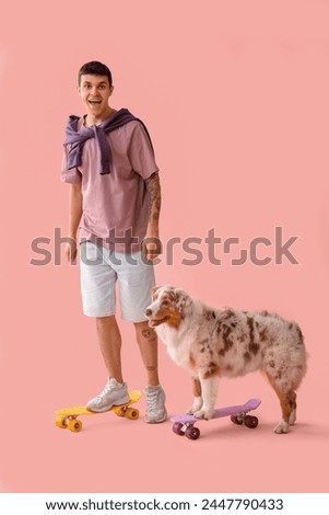 Young man with Australian Shepherd dog skating on pink background