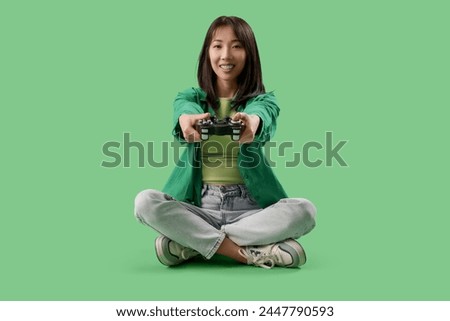 Happy Asian woman holding gamepad on green background