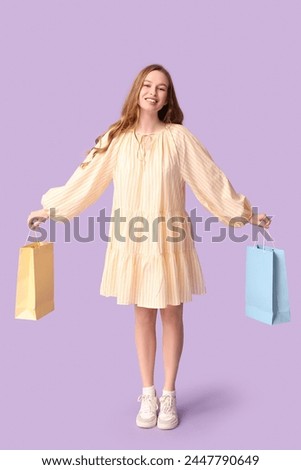 Happy young woman with shopping bags on lilac background