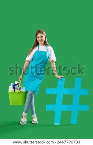 Female janitor with cleaning supplies and hashtag sign on green background