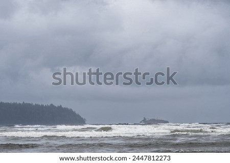 Large waves crash to shore at Deep Bay beach on a dreary and stormy day on Vancouver Island. Boyle Point lighthouse off the south coast of Denman Island is visible in the background. Royalty-Free Stock Photo #2447812273
