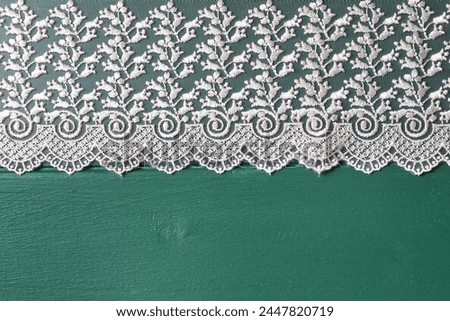 Beige lace on green wooden table, top view. Space for text