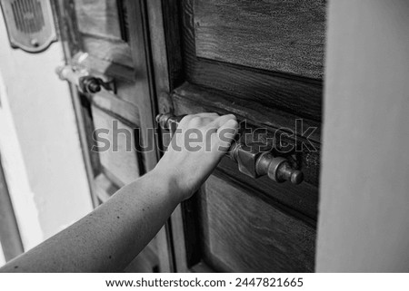 A wooden door and a hand on a massive metal handle. A woman's hand opens or closes the door. Close-up photo.