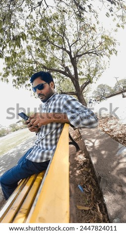 A Alone Person sitting in the Park bench and using Mobile phone