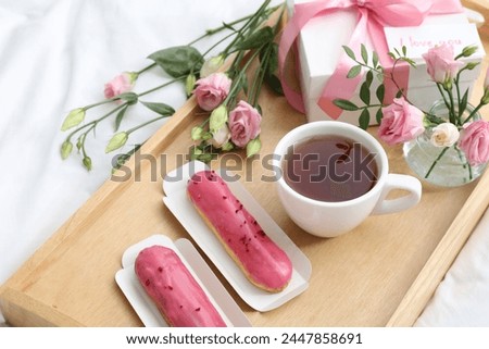 Tasty breakfast served in bed. Delicious eclairs, tea, gift box, flowers and card with phrase I Love You on tray