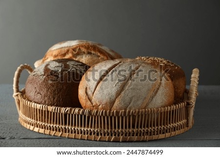 Wicker basket with different types of fresh bread on grey wooden table Royalty-Free Stock Photo #2447874499