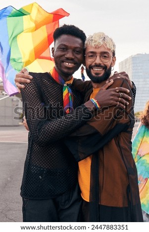 Cheerful portrait of male gay couple hugging while looking at camera smiling. Two men at pride parade celebrating the LGBTQIA month. Vertical photo with copy space. Royalty-Free Stock Photo #2447883351