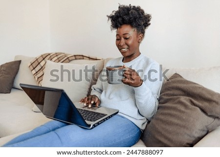 Happy African American woman having fun using laptop at home. Laughing watching funny online videos.