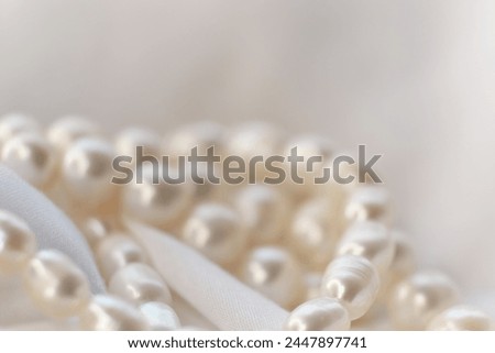 A string of pearls gracefully rests on a white backdrop, blurring softly at the edges. The image is a quaint juxtaposition to the sharp, high-definition visuals trending in today's digital landscape.