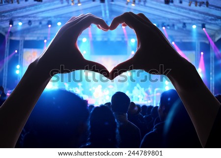 Crowd of people at during a concert  with a heart shaped hand shadow