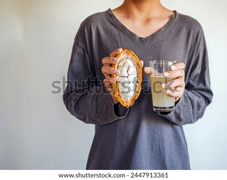 Fresh Cacao water in glass and half sliced ripe yellow cacao pod with white cocoa seed in the hands of boy teen, Cacao juice in glass, Healthy lifestyle