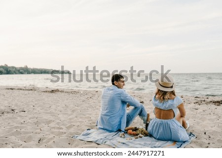 Man and woman having picnic date. Rear view of couple while sitting on picnic blanket on sand sea. Female and male on beach ocean and enjoying sunny summer day.  spending time together. Back view