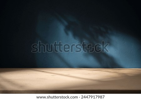 Empty table on dark blue texture wall background. Composition with organic shadow on the wall and light reflections. Mock up for presentation, branding products, cosmetics food or jewelry.