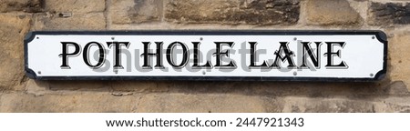Road sign on a stone wall giving its location as "Pot Hole Lane."
