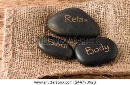Picture of three lava stones Relax, Soul and Body placed on jute cloth which is on the old worn wooden board with nice texture.