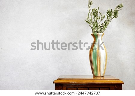 Modern summer still life photo. vase with green olive tree branch on wood table near gray wall background. Empty copy space. Elegant lifestyle Mediterranean scene