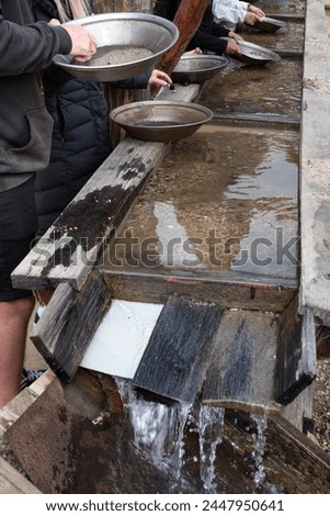 People searching for gold with iron pans in running water through a wooden gutter. Gold panning Royalty-Free Stock Photo #2447950641