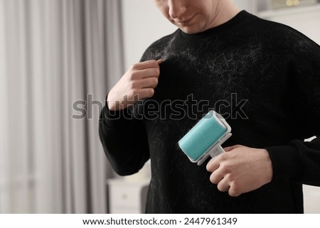 Pet shedding. Man with lint roller removing dog's hair from sweater at home, closeup