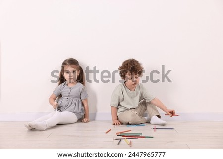 Cute little children with colorful pencils near white wall indoors