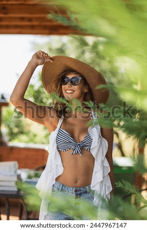 A beautiful smiling woman is wearing a stylish hat and sunglasses posing for a picture while goes to the beach on a sunny day.