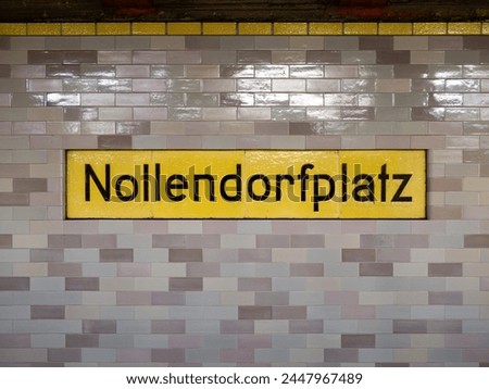 Nollendorfplatz station sign in Berlin. The location signage of the public transportation is part of the underground. The wall is tiled and the label is yellow.
