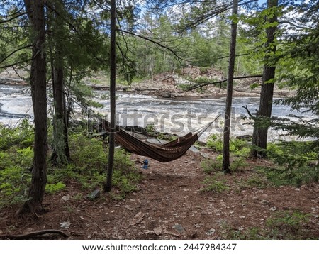 A woman lays on a hammock beside a raging river in the forest Royalty-Free Stock Photo #2447984347