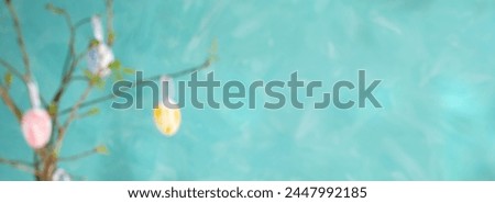 Blurred holiday banner with Easter tree. Decorative pastel color eggs hanging on spring twigs with young leaves on turquoise background. Creative defocused Easter image with free space for text.