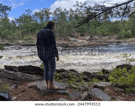 A woman stands barefoot beside a rapid on a river Royalty-Free Stock Photo #2447993513