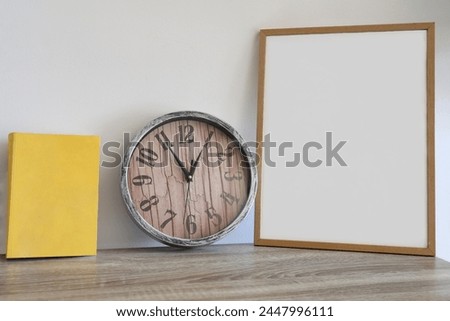 blank mockup frame. home desk with yellow book, round watch and mock up wooden frame. template for photo image, picture. white wall on background. empty copy space for inscription. interior front view